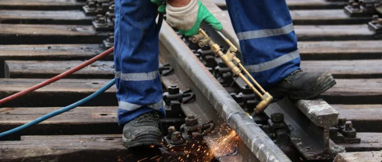 Close up image of a track worker in blue pants working on the rail
