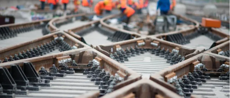Close up image of multiple tracks converging at multiple points with orange track workers in the distance