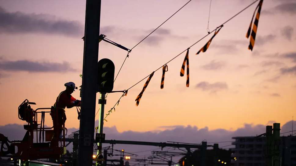 Worker replacing the overhead electrical system in front of a pastel coloured sky