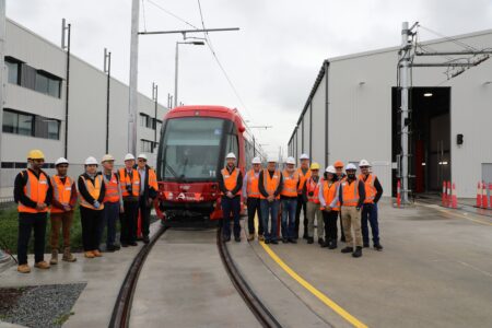 Photo of RTSA members in high vis vests and hard hats standing beside a red CAF Tram at the PLR Depot